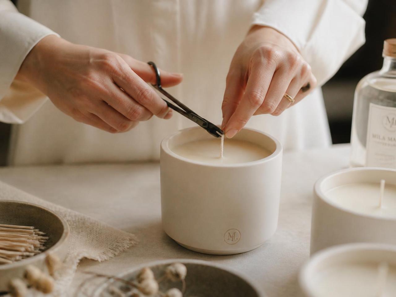Hands centring and trimming a cotton wick on a curing candle